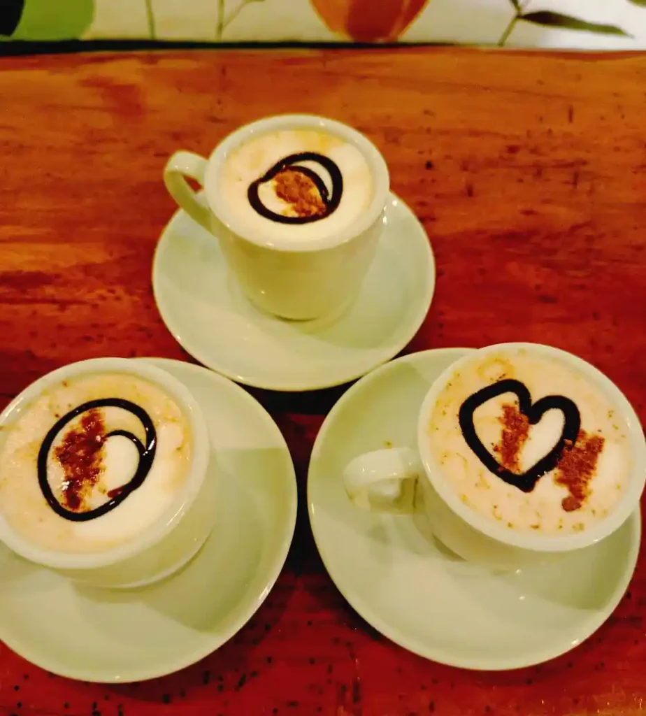 Tres bebidas de café decoradas sobre una mesa de madera en Mi Refugio Café y Arte de Calarcá