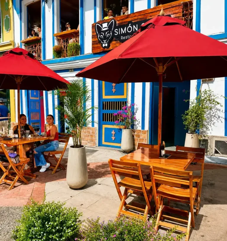 Terraza con mesas, sombrillas y fachada colorida de Simon Simon Restaurante Cafe en Calarca