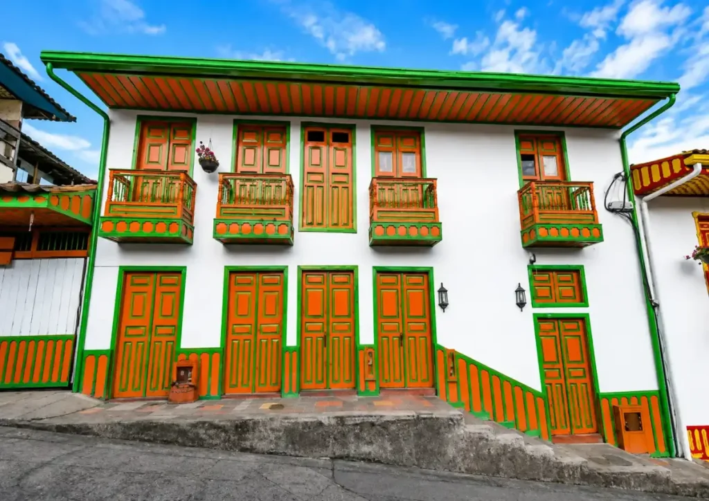 Casa tradicional de fachada blanca con puertas, ventanas y balcon verde en Salento, Quindío