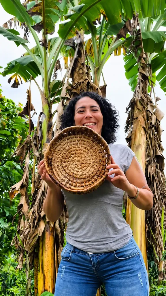 Mujer sosteniendo una bandeja tejida con fibra vegetal entre plantas de plátano