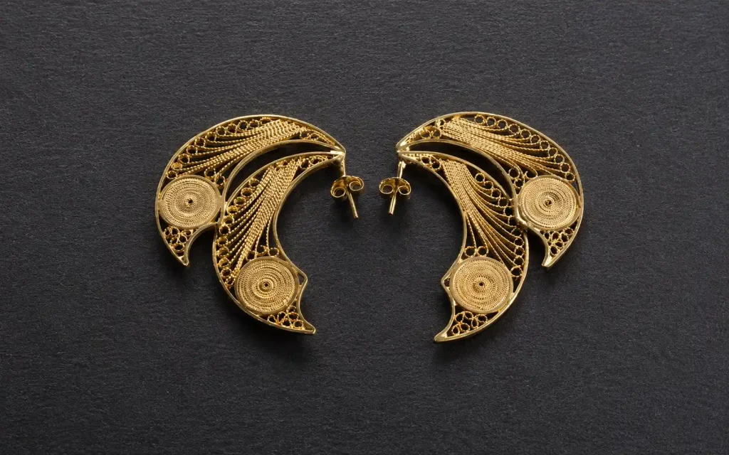 Par de aretes dorados elaborados con finos hilos metálicos sobre fondo oscuro